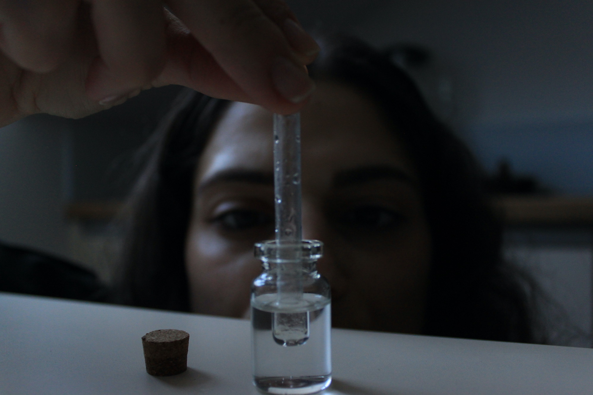 A young brunette woman placing a glass dropper inside a tiny transparent glass jar filled with rainwater. 